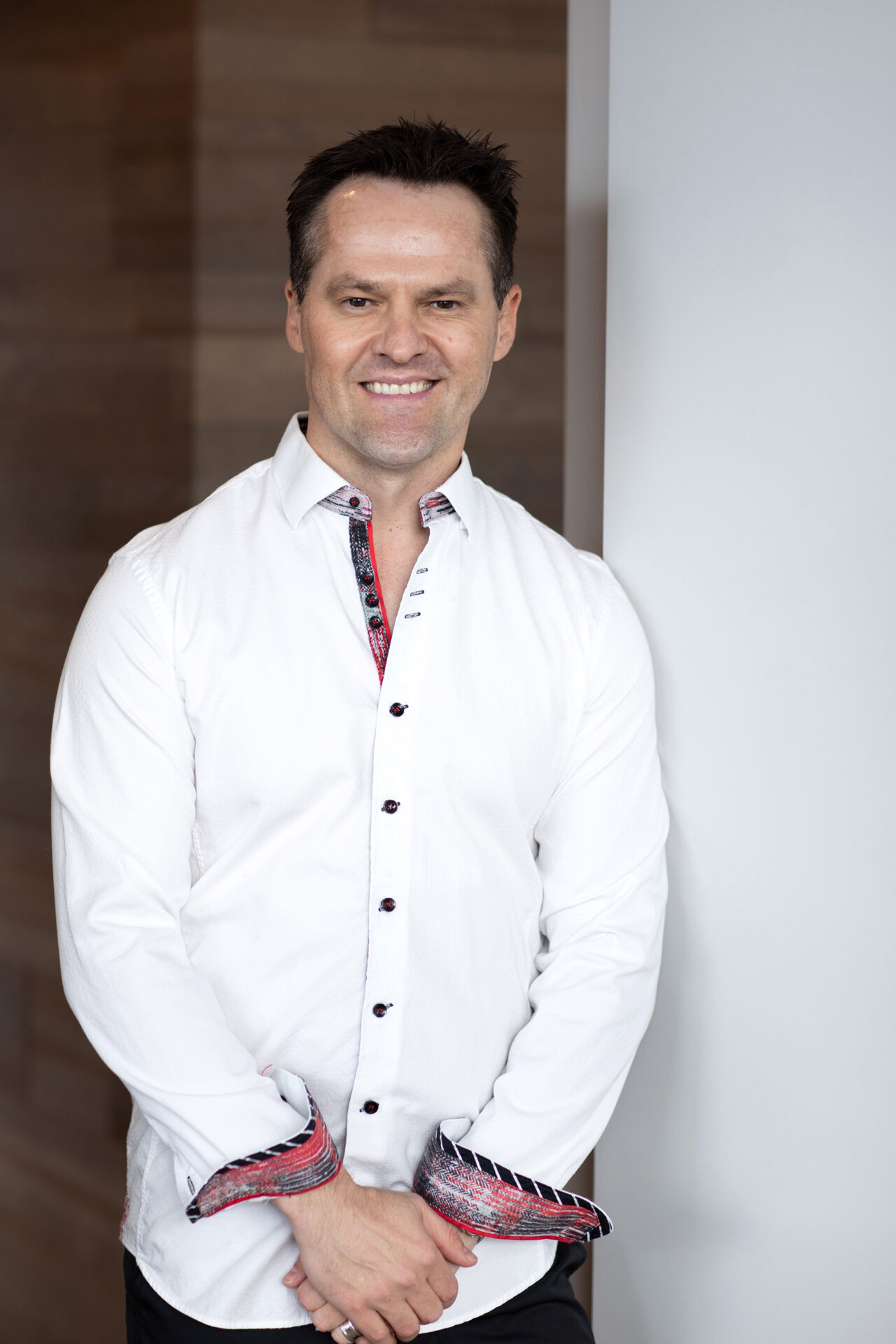 An image of Dr Ben Wiese in a white button-up shirt standing next to a white wall, a headshot for one of the skin cancer awareness month interviews