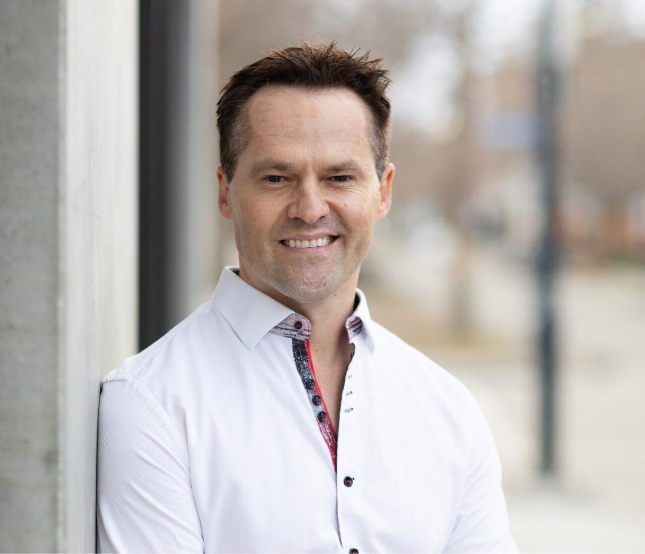 Headshot of Dr Ben - a white man with short brown hair standing against a wall in a white shirt. 