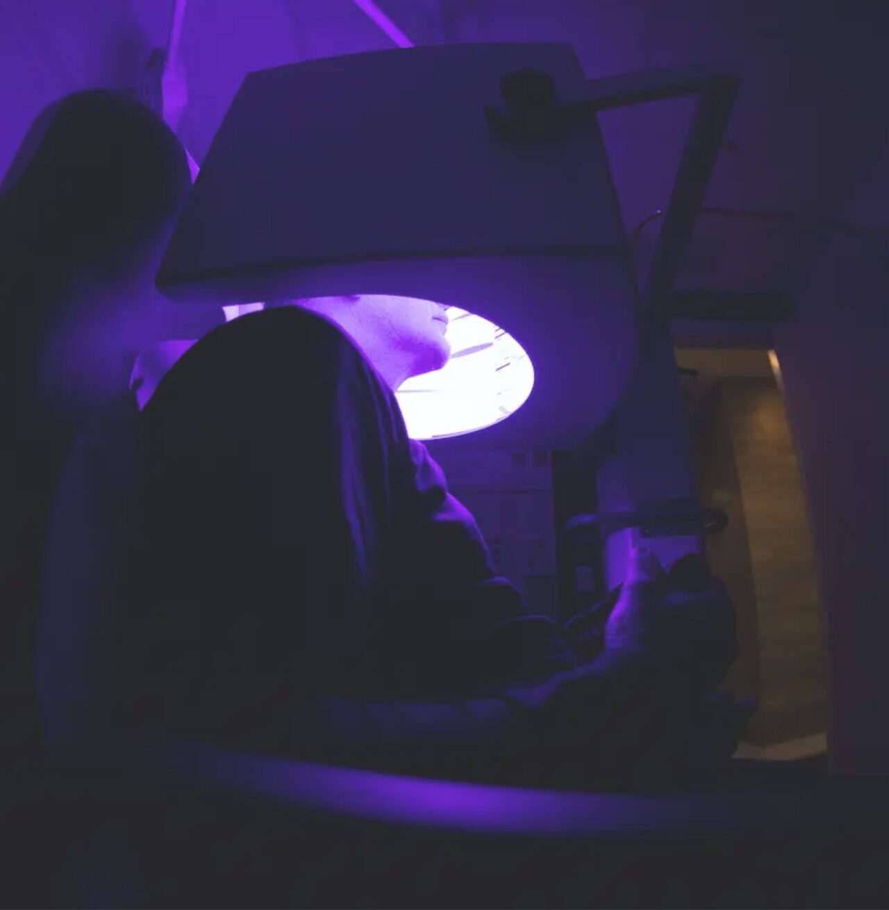 A dark image with a purple tinge of a person sitting inside an upright diagnostic machine.