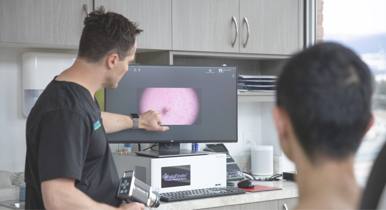 Dr Ben showing a patient a skin spot on a screen in his office. Back of the patient's head is out of focus in the foreground.